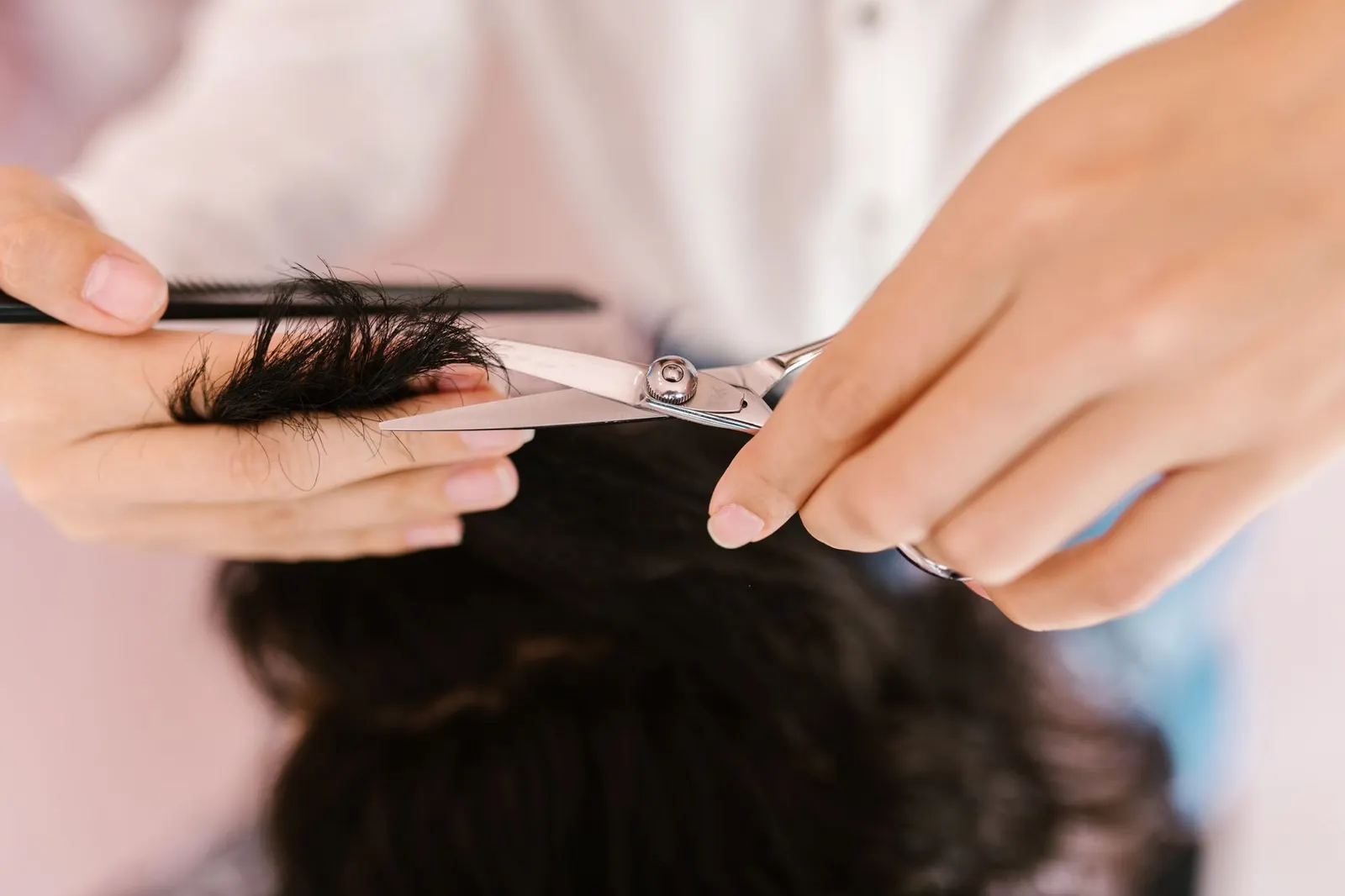 Gros plan de mains coupant des cheveux au ciseau en salon